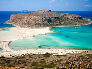 A coastal landscape with a rocky island, clear turquoise waters, and a sandy beach.