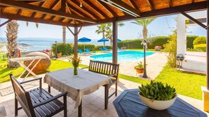 A covered outdoor area with a pool, lounge chairs, and a table with a plant. - Villa Pelagos Large Private Pool Walk to Beach Sea Views A C Wifi - 2429 (Pomos)