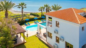A modern building with a swimming pool, sun loungers, and a view of the sea. - Villa Pelagos Large Private Pool Walk to Beach Sea Views A C Wifi - 2429 (Pomos)