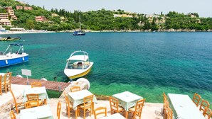 Un espace de restauration en bord de mer, avec des tables et des chaises, des bateaux sur l’eau et des bâtiments en arrière-plan.