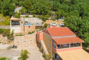 Un bâtiment en pierre avec un toit recouvert de tuiles rouges, une piscine et une voiture garée à proximité.