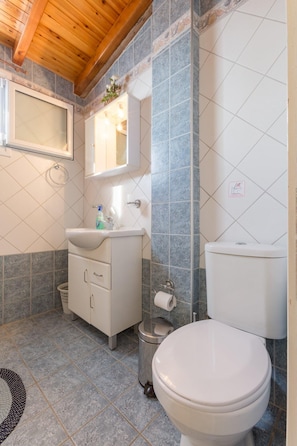 Une salle de bain avec des toilettes blanches, un lavabo avec un miroir au-dessus et une poubelle.