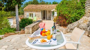 Una casa de piedra con tejado de baldosas, una mesa de comedor con cubierta de vidrio y una variedad de frutas y bebidas sobre la mesa.