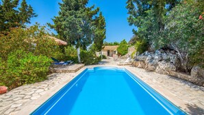 Una piscina rectangular con borde de piedra, rodeada de follaje y árboles.
