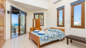 Un dormitorio con cama, un banco de madera, cómoda y balcón con mesa y sillas.