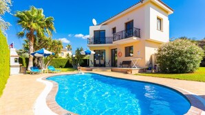 Una casa de dos pisos con piscina, muebles de jardín y un jardín.