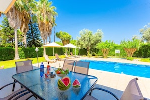A poolside area with a glass table, chairs, umbrellas, and a sign prohibiting diving.