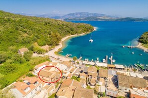Ein Küstendorf mit traditionellen Häusern, einem Yachthafen und freiem Blick auf das Meer und die dahinterliegenden Berge.