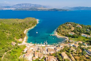 Vista aérea de un pueblo costero con un puerto deportivo, rodeado de colinas y un mar azul y despejado.