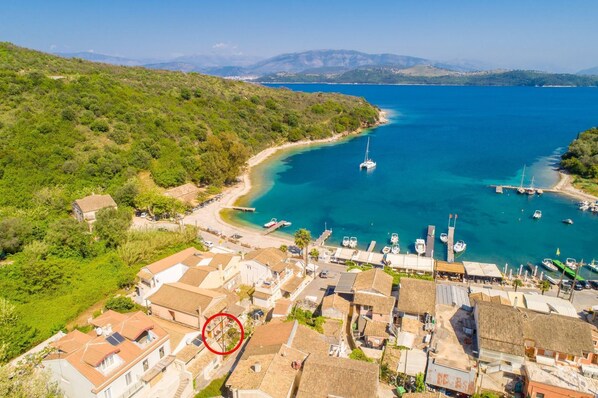 Un pueblo costero con edificios de tejas de arcilla, un puerto deportivo con barcos y colinas y montañas al fondo.