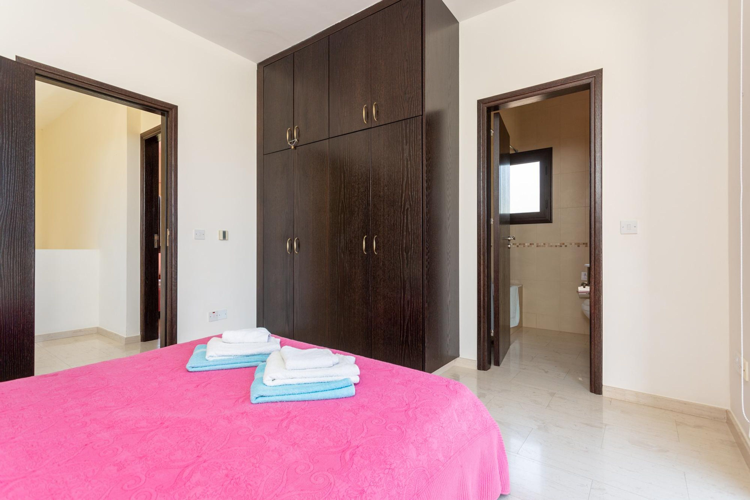 A bedroom with a large bed, dark wooden wardrobe, and a bathroom visible through an open door.
