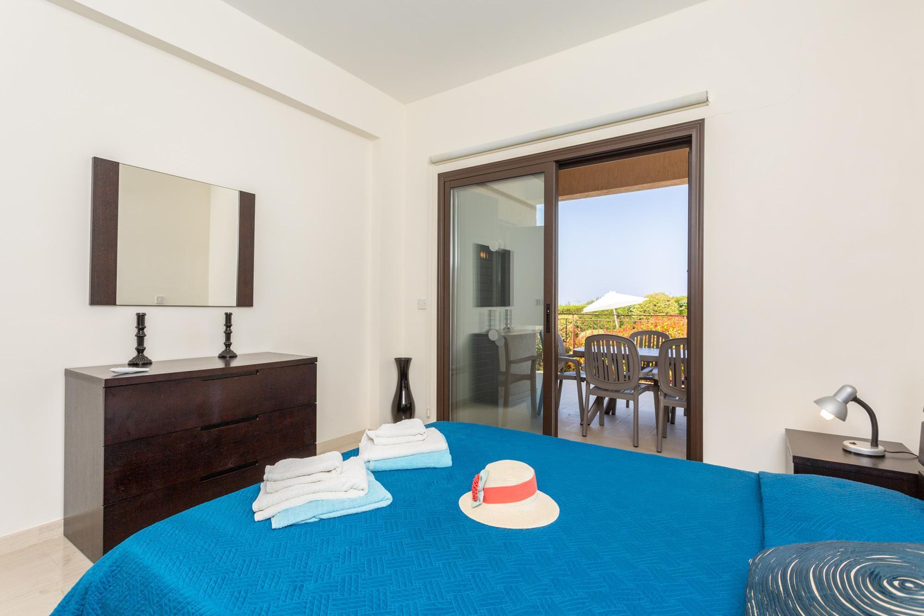 A bedroom with a large bed, a dresser, a mirror, a nightstand, and a view of the outside balcony.