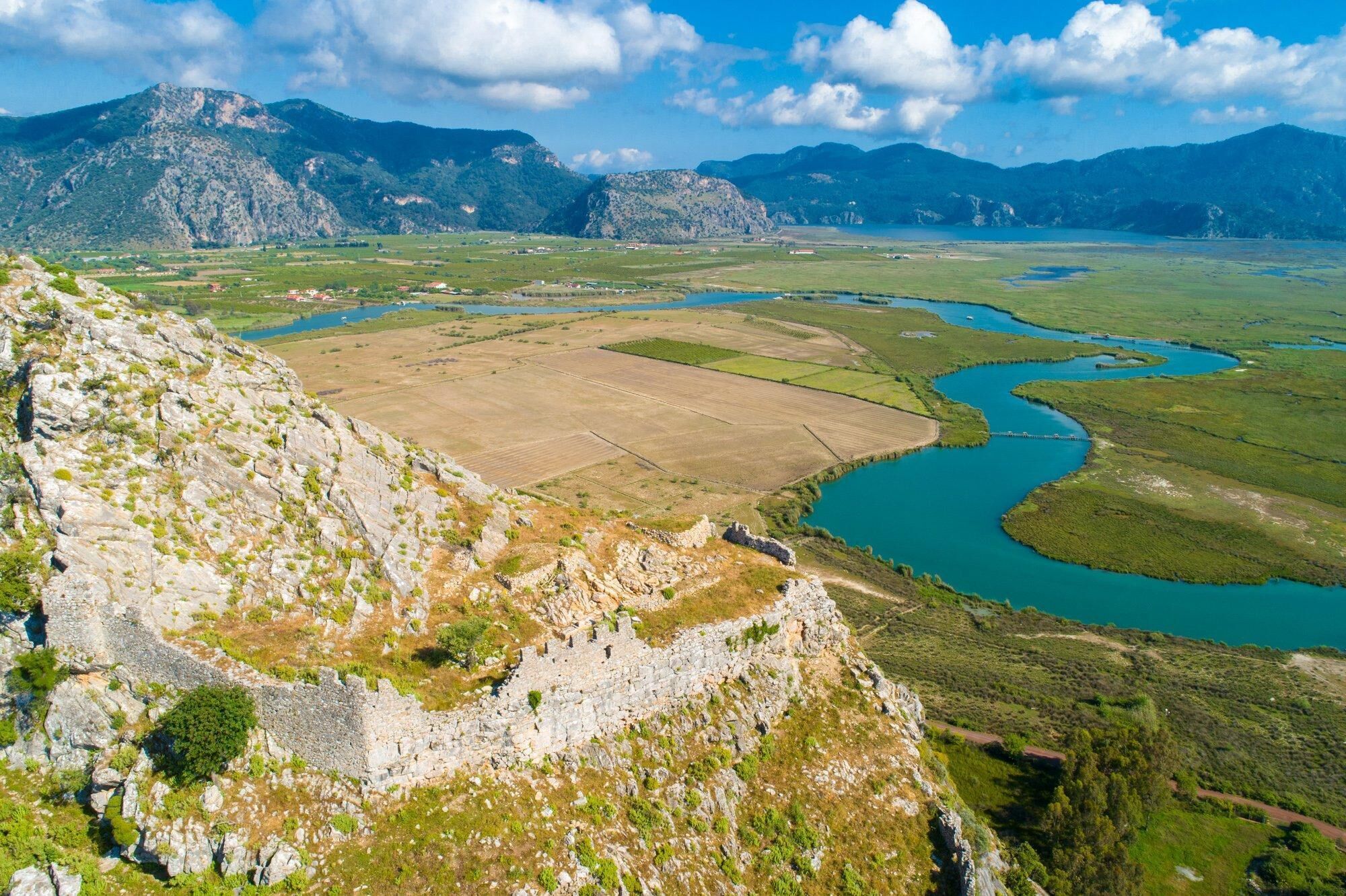 A mountainous landscape with a river, fields, and a stone structure.