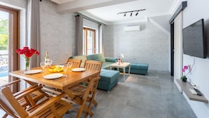 Een moderne woonkamer met een houten eettafel, een groene bank en een aan de muur bevestigde televisie.