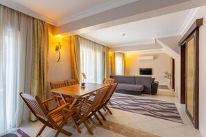 Une chambre d’hôtel comprenant un coin repas, un canapé, une télévision et une grande fenêtre avec des rideaux.