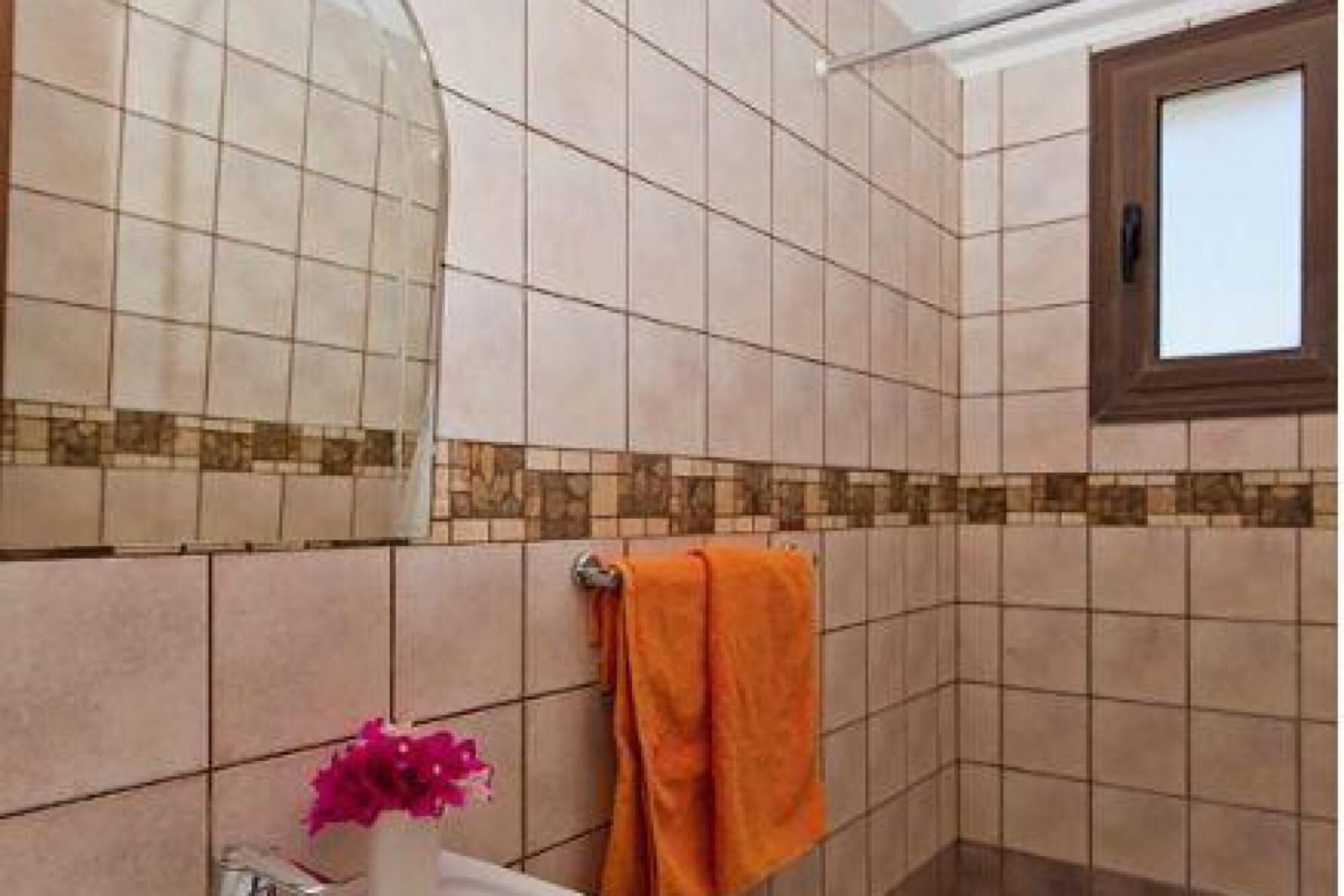 Une salle de bain avec des carreaux de couleur beige, une fenêtre et une serviette orange.