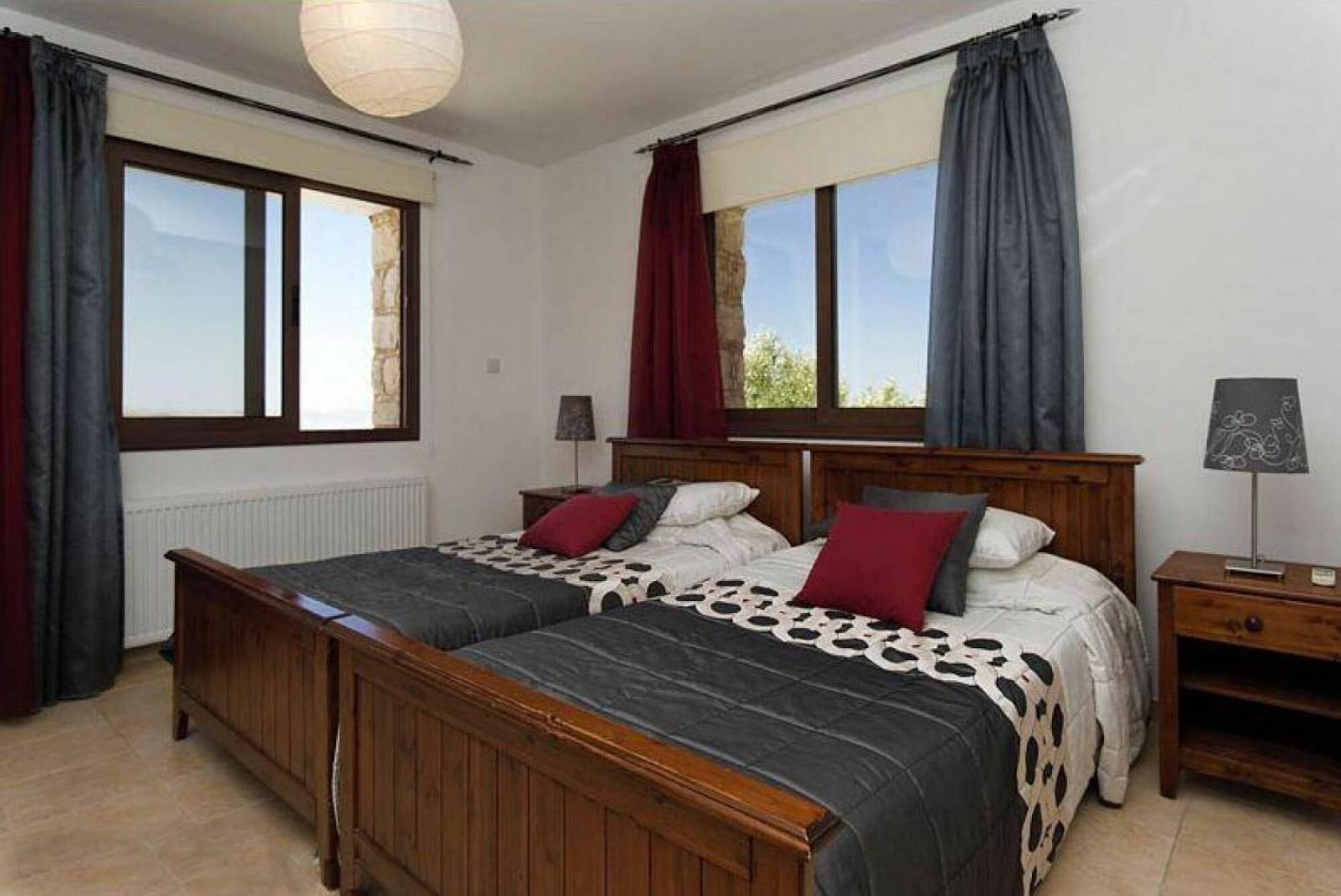 Una cama doble con colcha estampada, dos mesitas de noche, una lámpara y vistas al exterior a través de amplios ventanales.