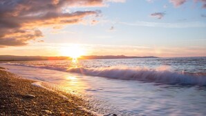 A beach scene with the sun setting over the ocean, waves gently lapping the shore, and a clear sky with scattered clouds. - Villa Heaven Large Private Pool Sea Views A C Wifi Eco-friendly - 2645 (Peristerona)