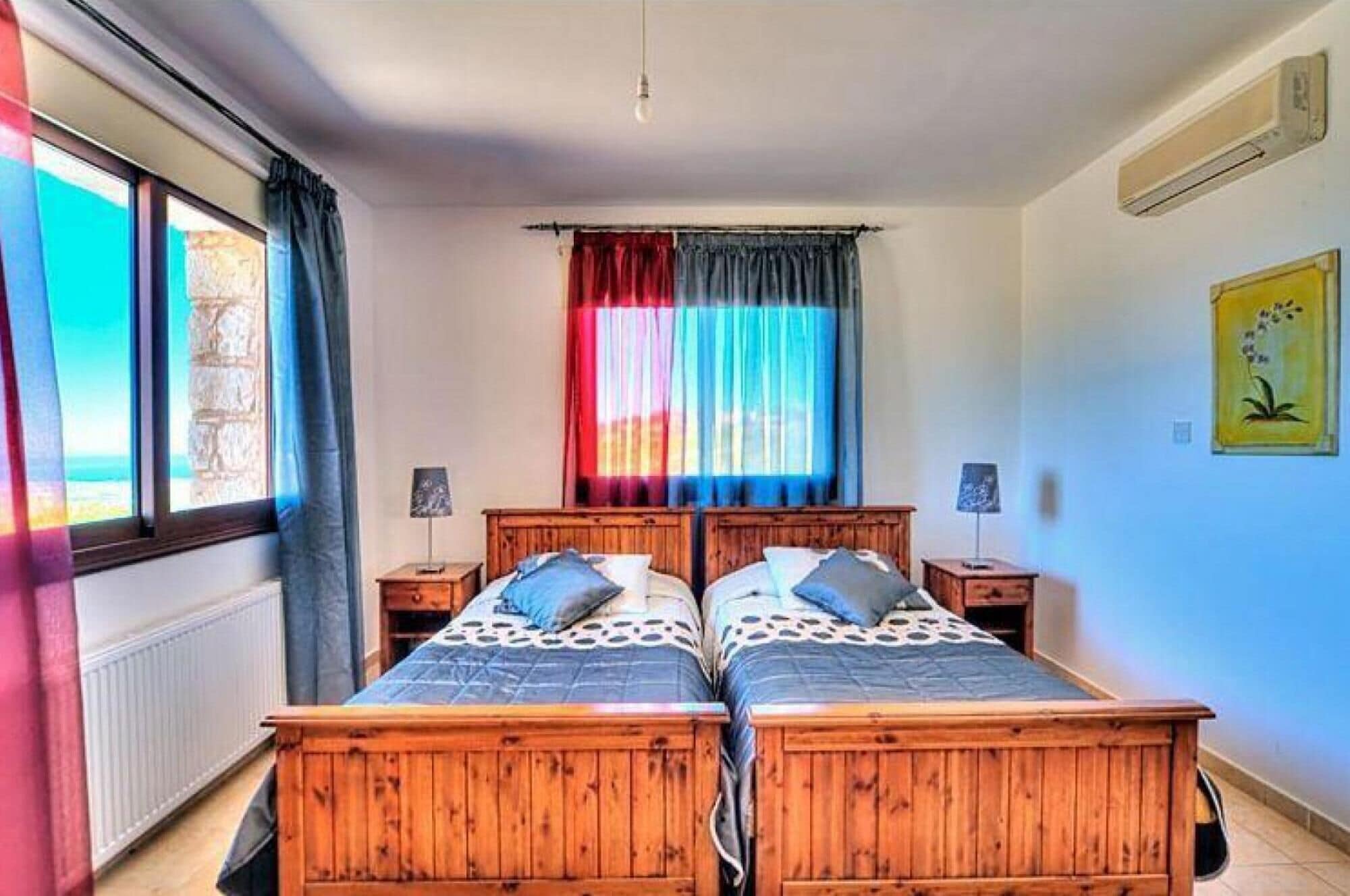 A room with two wooden beds, a window with curtains, a radiator, and a wall-mounted air conditioner.