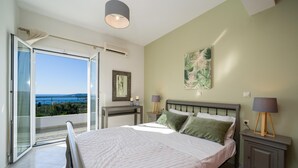 A bedroom with a bed, bedside tables, a nightstand, a window with a view, and a ceiling light. - Villa Erasmia Large Private Pool Walk to Beach Sea Views A C Wifi - 2646 (Kefalonia)