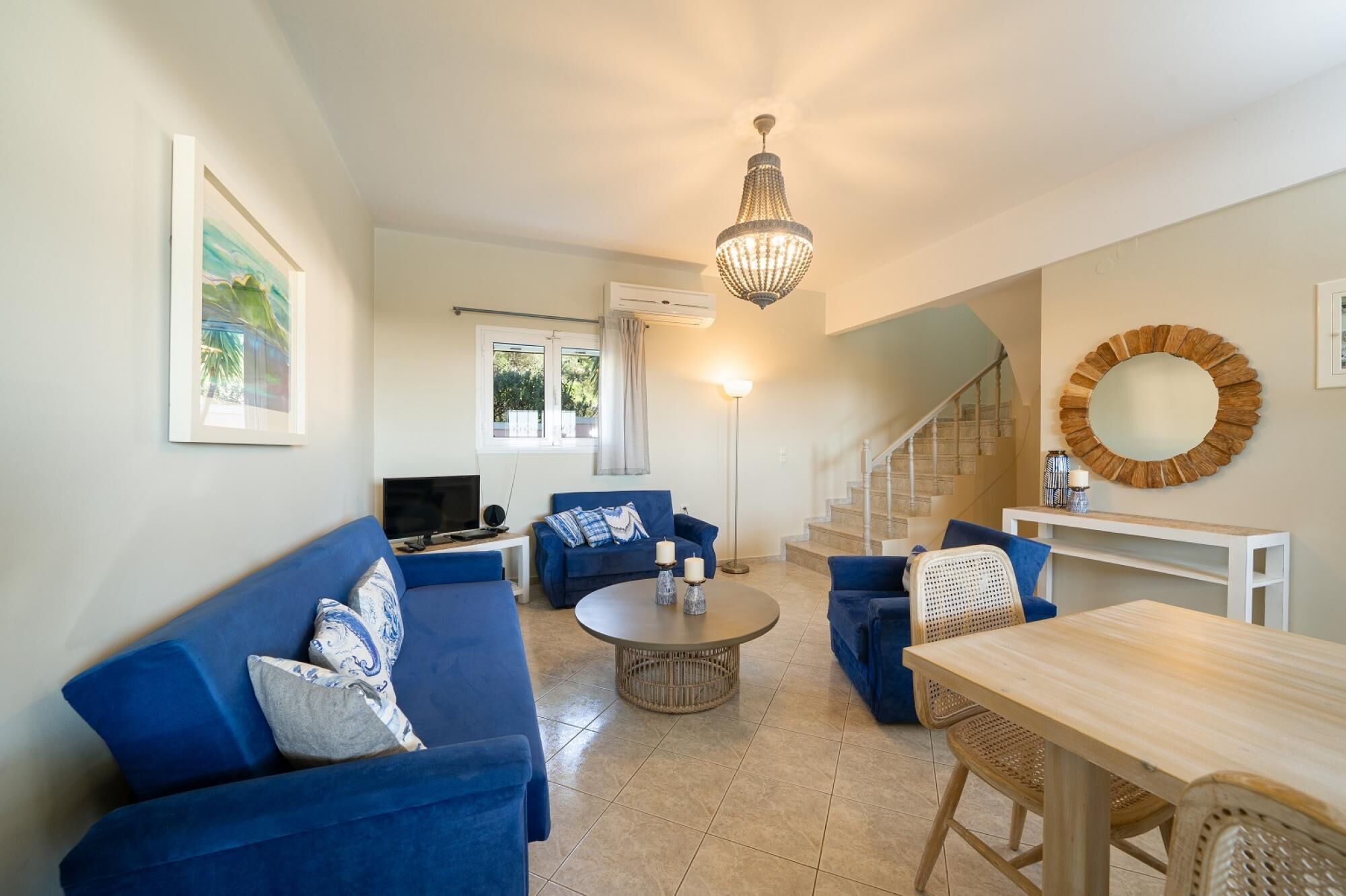 Un salon avec un canapé bleu, une table basse ronde, un téléviseur et un escalier menant à un autre niveau.