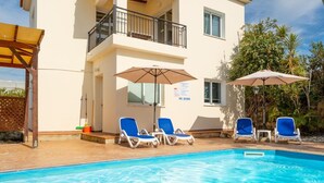 Un edificio de dos pisos con piscina, sillones azules y sombrillas.