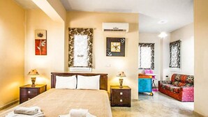 Una habitación de hotel con una cama grande, dos mesitas de noche, un equipo de aire acondicionado y un sofá al fondo.