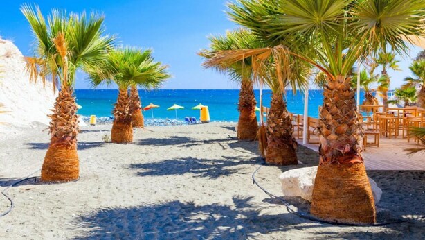 Een strand met palmbomen, een zandpad en een houten terras met stoelen.