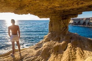 A person standing under a natural rock formation by the sea, overlooking the ocean. - Villa Argaka Sunset Large Private Pool Walk to Beach Sea Views A C Wifi Eco-friendly - 2760 (Argaka)
