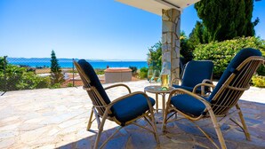 A patio with wicker chairs and a table, overlooking a scenic view of the sea.
