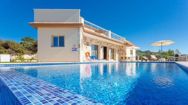 A swimming pool with a tiled edge, a building with a balcony, and outdoor seating. - Villa Christel Large Private Pool A C Wifi Eco-friendly - 2761 (Peristerona)