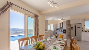 A dining area with a table set for four, a view of the sea, and a kitchen with modern appliances. - Villa Christel Large Private Pool A C Wifi Eco-friendly - 2761 (Peristerona)