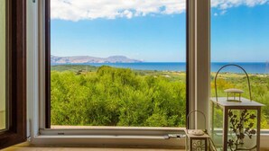 Ein Zimmer mit großem Fenster und Blick auf eine grüne Landschaft sowie das Meer.