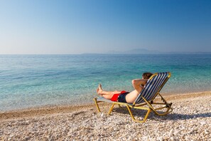 A person relaxing on a beach chair facing the sea.