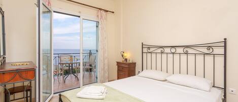 A bedroom with a bed, a desk, and a balcony with a view.