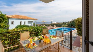 Un balcon avec une table préparée pour le petit-déjeuner, donnant sur une piscine et un bâtiment dont le toit est recouvert de tuiles.