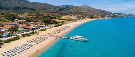 A coastal town with a beach, a pier, and a yacht docked at the pier.