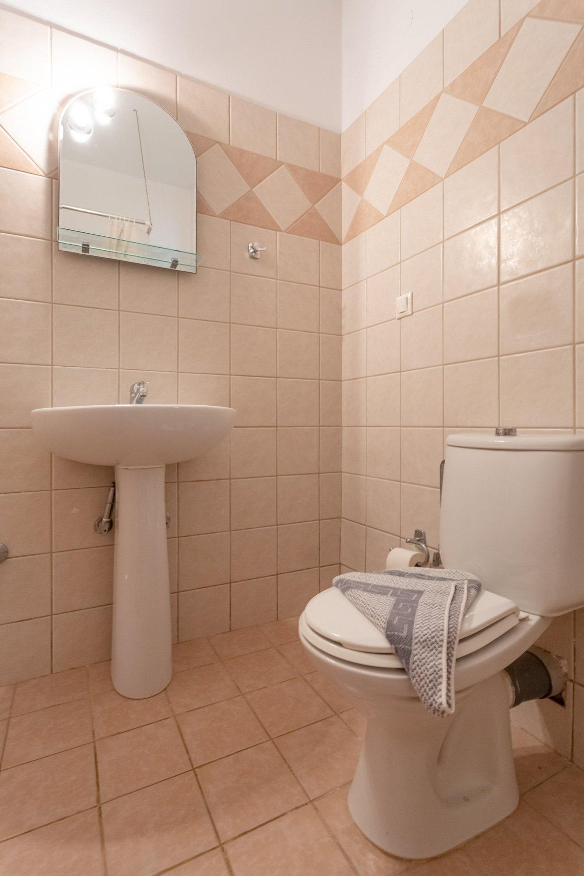 A bathroom with a pedestal sink, toilet, and a mirror.