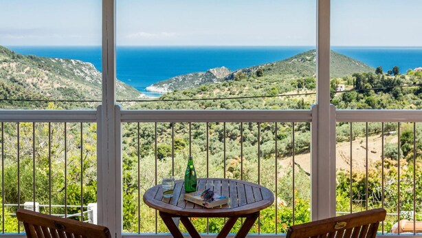 A balcony with a wooden table and chairs, overlooking a coastal landscape with hills and the sea. - Villa Glafki Large Private Pool Sea Views A C Wifi - 2829 (Skopelos)