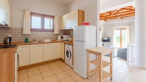 A compact kitchen with a washing machine, a refrigerator, and a wooden table. - Villa Glafki Large Private Pool Sea Views A C Wifi - 2829 (Skopelos)