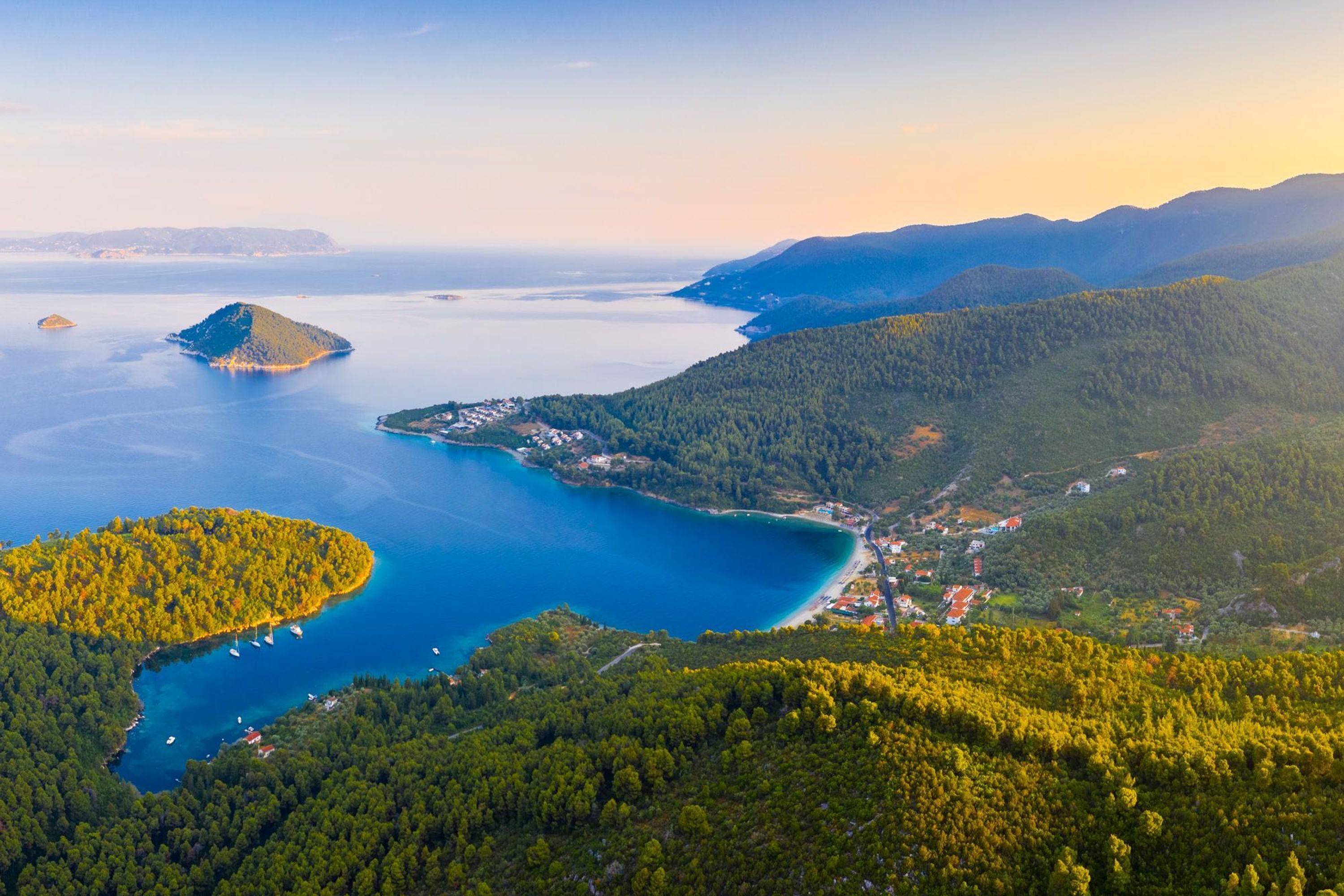 Vue aérienne d’une zone côtière avec une petite île, une baie et des collines environnantes.