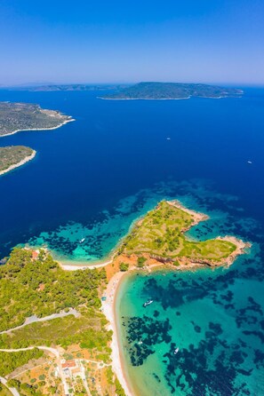 Vue aérienne d’une zone côtière avec des eaux d’un bleu limpide, une petite île verdoyante et une plage où se trouvent des bateaux.