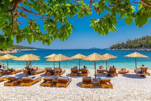 A beach with sun loungers and thatched umbrellas, clear blue water, and a rocky coastline. - Villa Tassoula Large Private Pool Walk to Beach Wifi - 2830 (Alonissos)