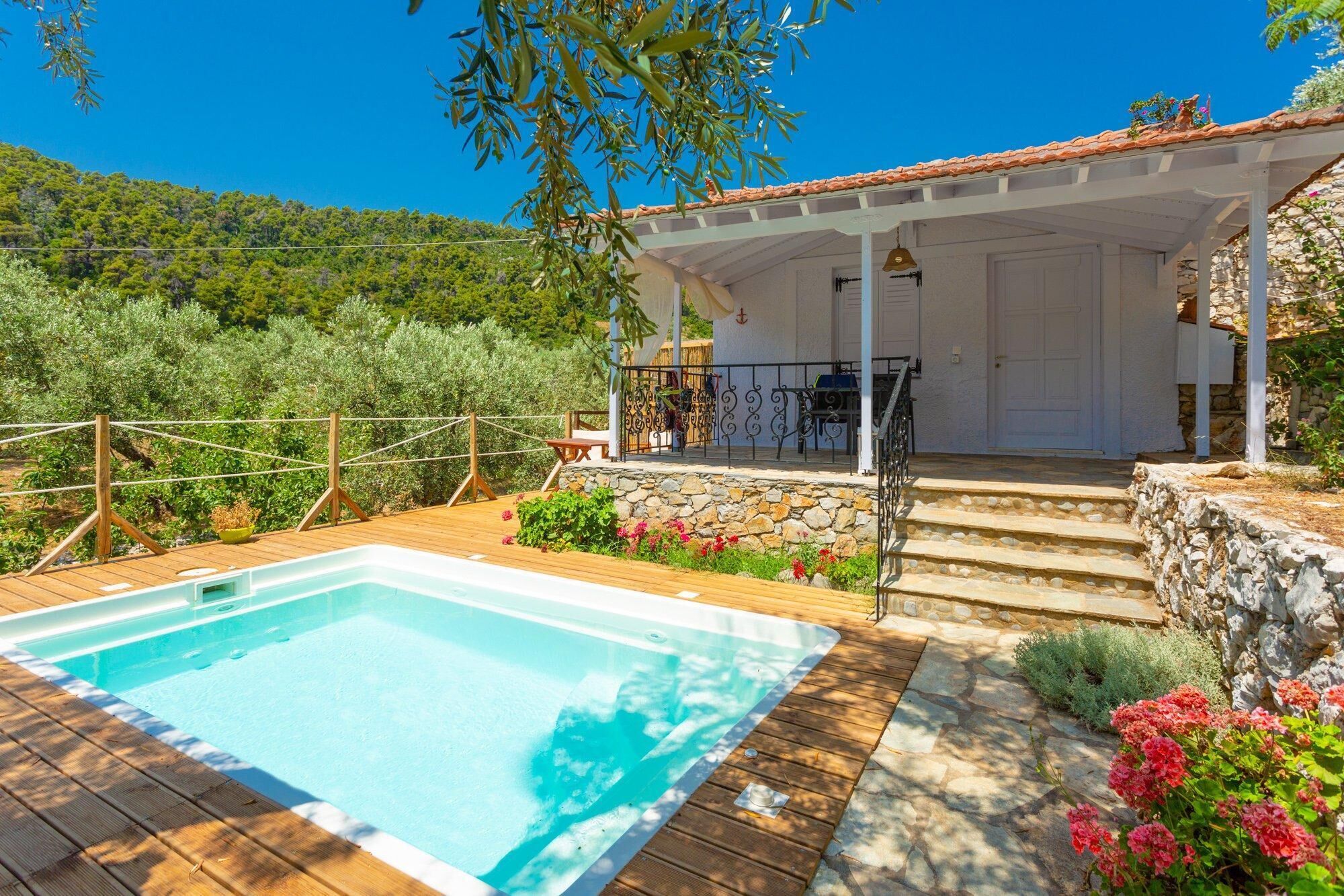 A pool area with a wooden deck, a stone wall, and a covered seating area with outdoor furniture.