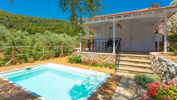 A pool area with a wooden deck, a stone wall, and a covered seating area with outdoor furniture.