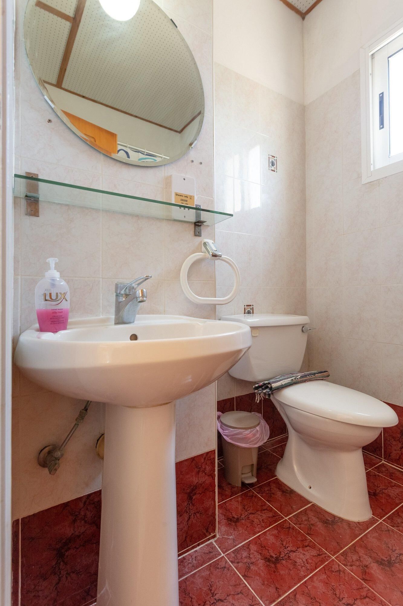 A bathroom with a pedestal sink, a toilet, and a glass shelf above the sink.