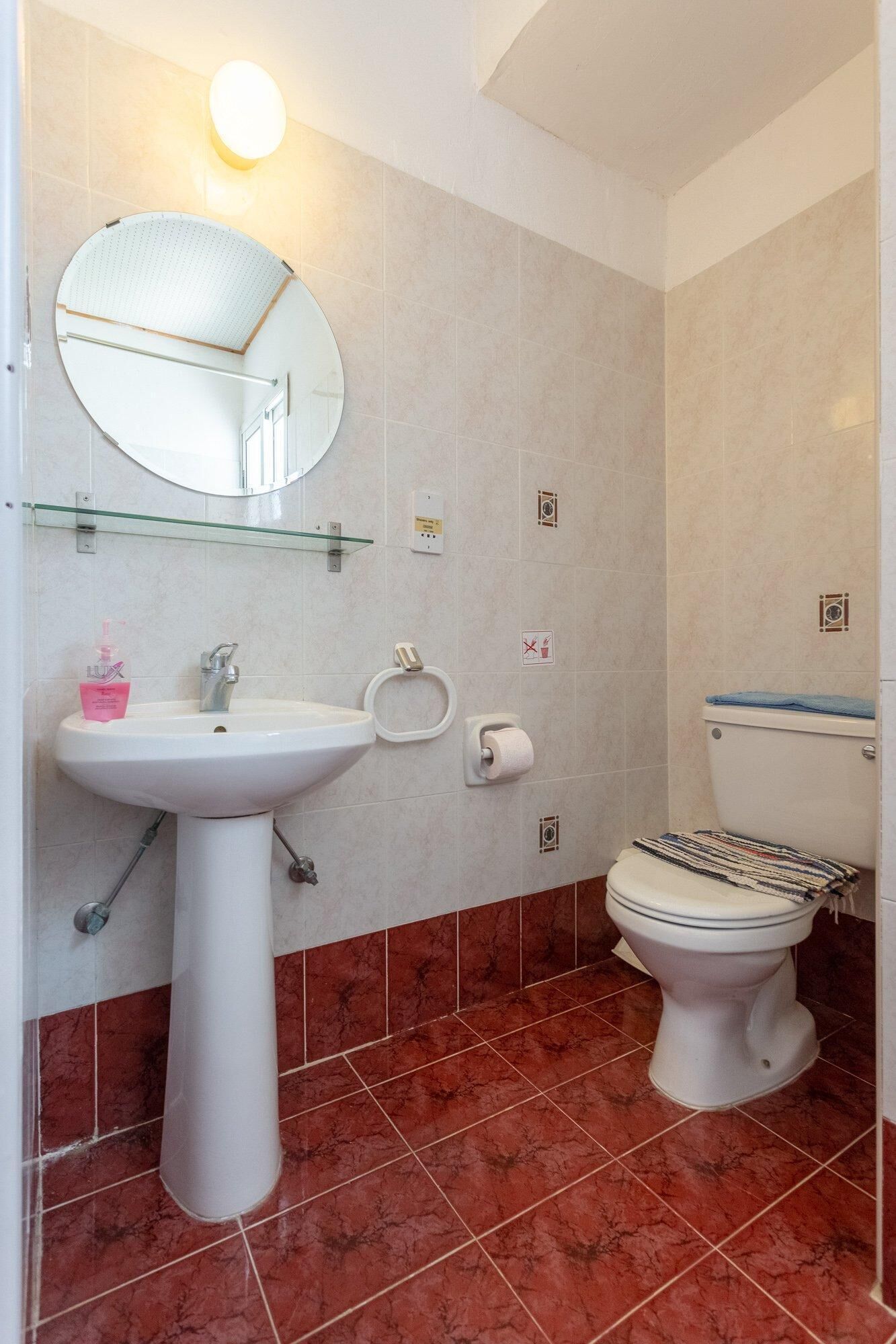 Ein Badezimmer mit Waschbecken, Spiegel und Toilette. Darüber befindet sich ein Glasregal, und eine Handtuchstange ist an der Wand montiert.