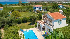 A residential area with a swimming pool, a small house with a red-tiled roof, and a view of the sea and mountains in the background. - Sun Beach Villa Thio Large Private Pool Walk to Beach A C Wifi Car Not Required - 2840 (Polis)