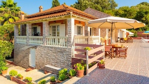 Un bâtiment en pierre avec un toit en tuiles, un balcon doté d’une balustrade et un espace extérieur aménagé avec des parasols.