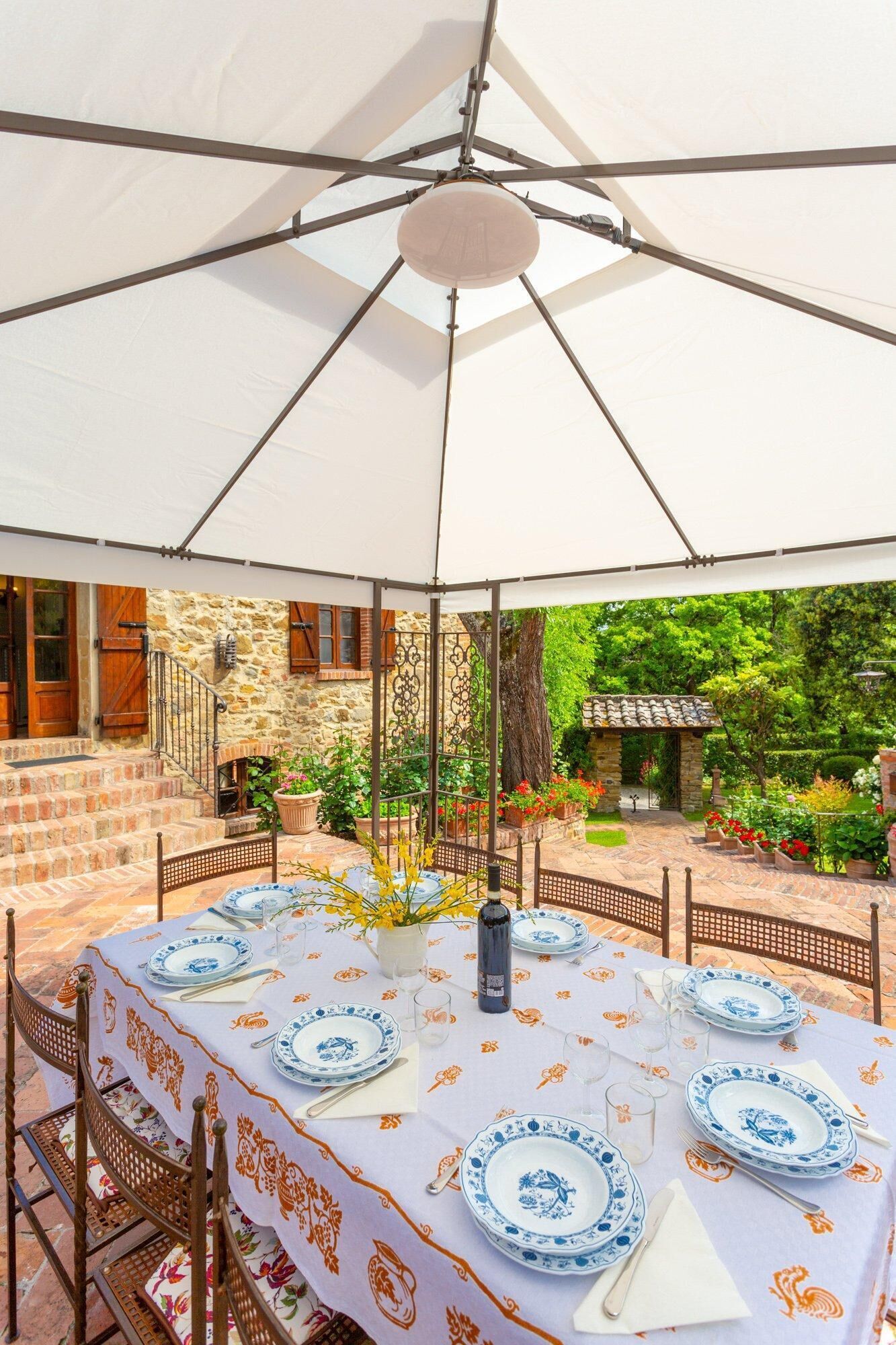 Un espace de restauration en plein air avec une table dressée pour quatre personnes, entouré de murs en pierre et d’un jardin.